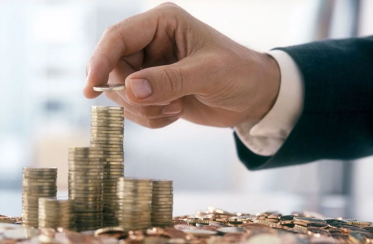A hand placing a coin on growing stacks of coins